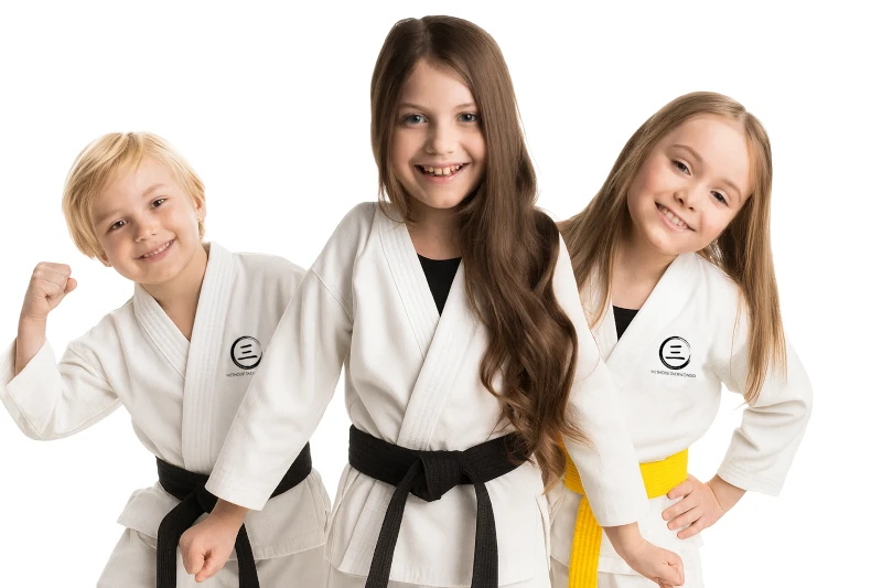 Drei Kinder in Karateanzügen mit farbigen Gürteln lächeln selbstbewusst in die Kamera.